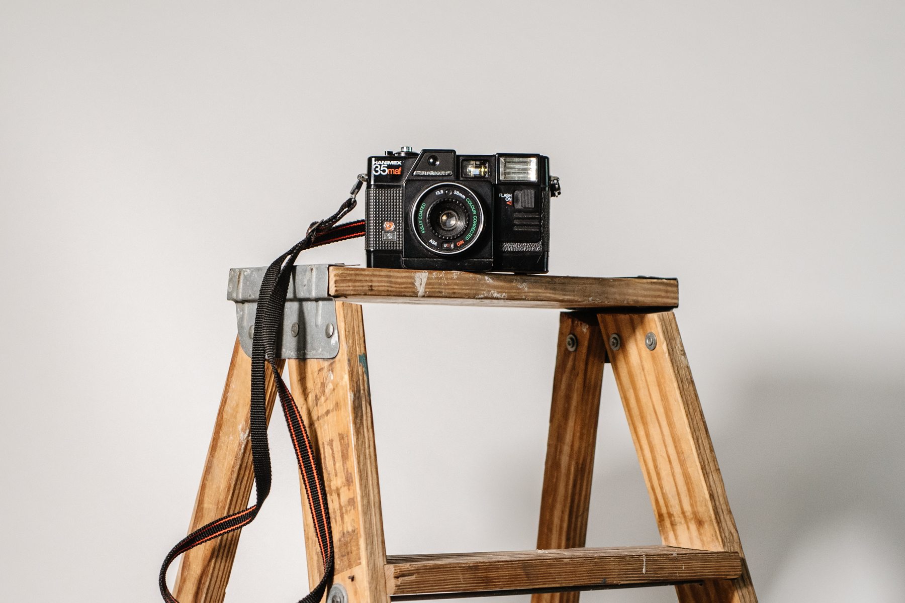 An old film camera resting on the top of a wooden step ladder
