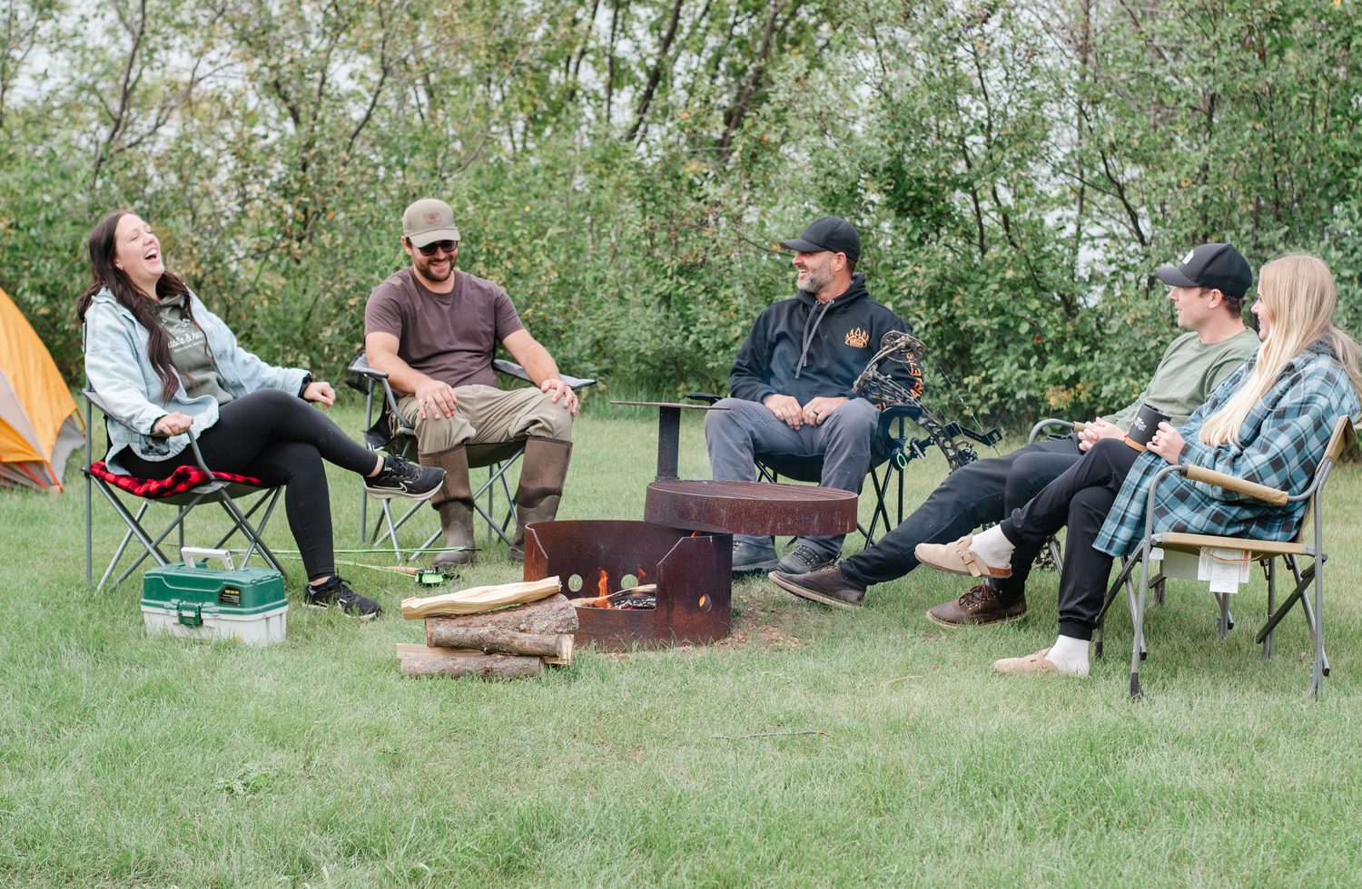 Five friends laughing together around a campfire at a rural campground