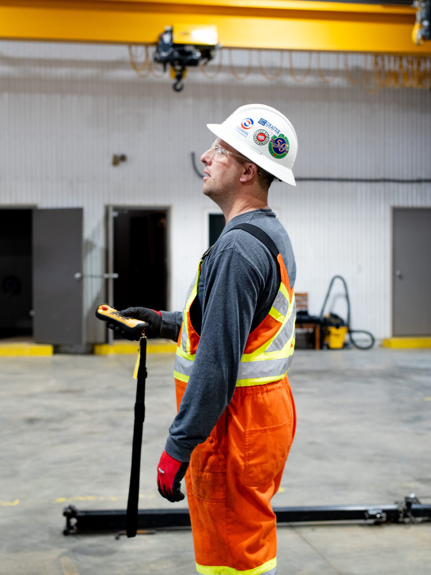 An operator in hi-vis coveralls watching an overhead crane move a load in his shop