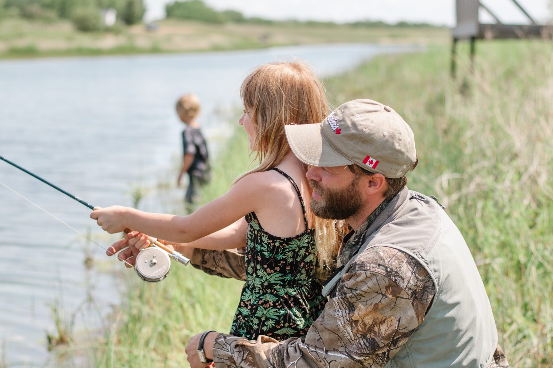 A father showing his daughter how to cast a fly rod on the bank of a county lake