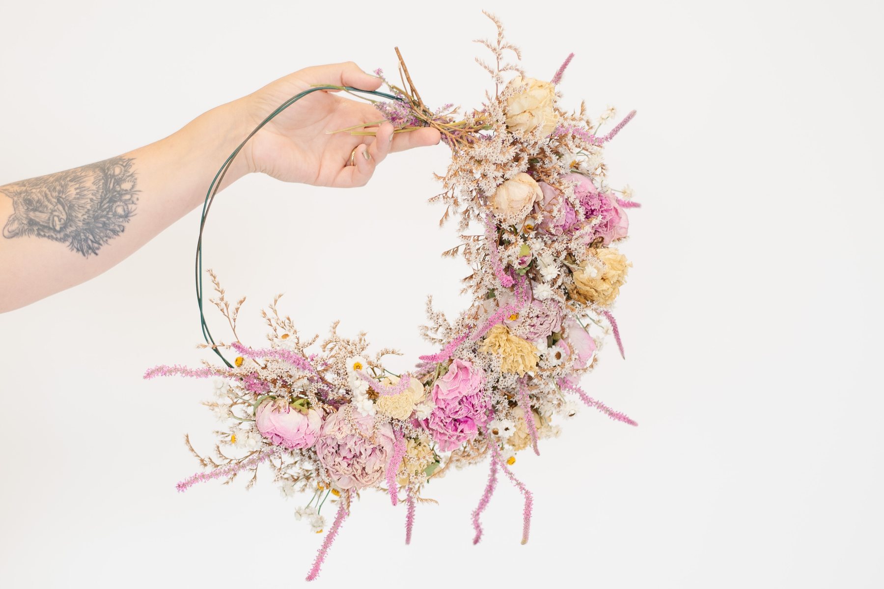 A dried flower wreath held up against a plain wall for a maker's product photography